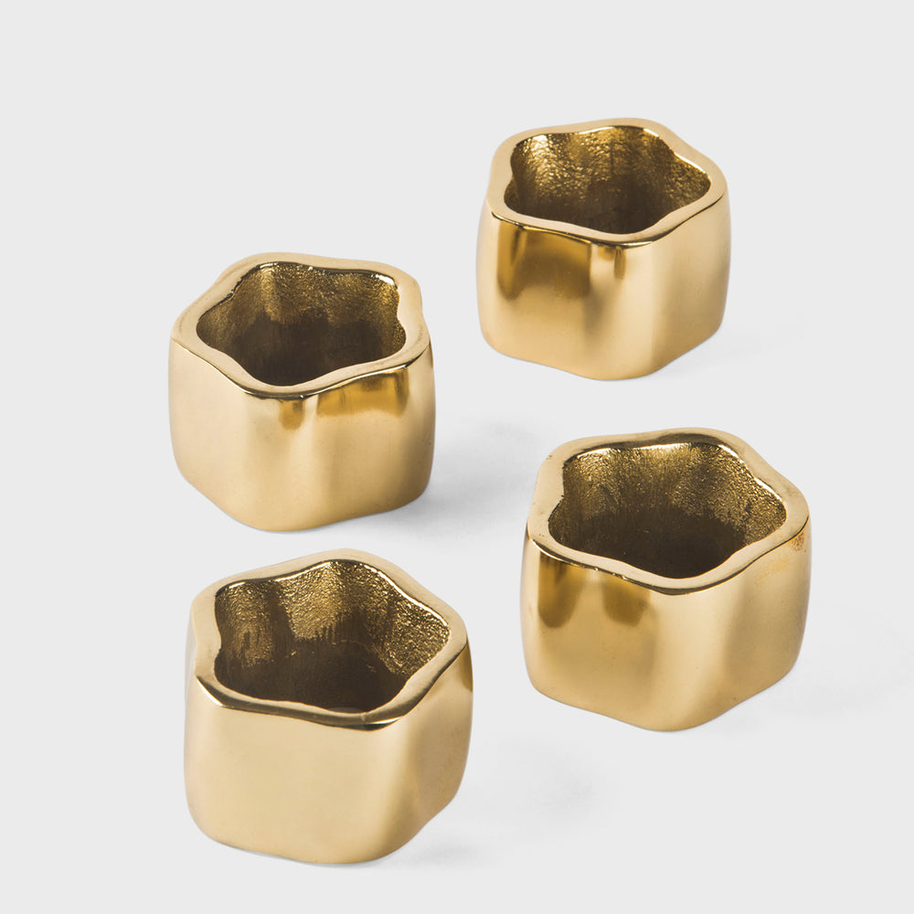 Set of four thick, sculpted gold napkin rings with a modern hexagonal-inspired shape on a white linen napkin.