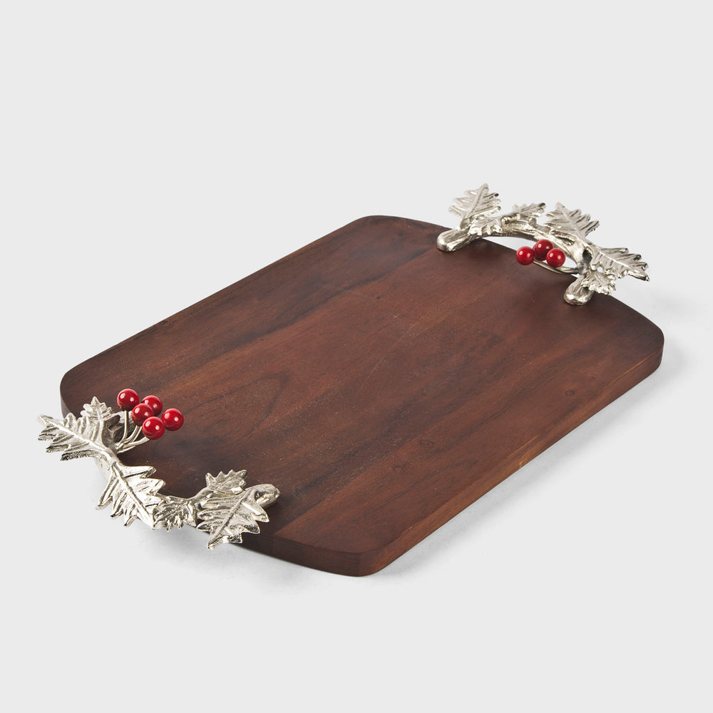 Wooden cutting board with silver handles featuring leaves and red berries on a light gray background