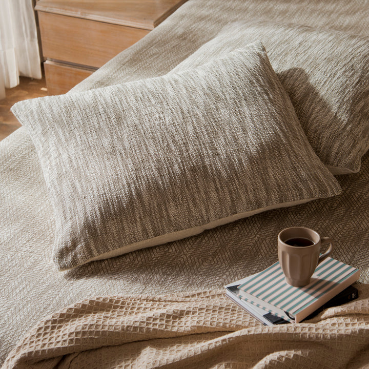 Earthy standard shams styled on a bed layered with quilt and cushions
