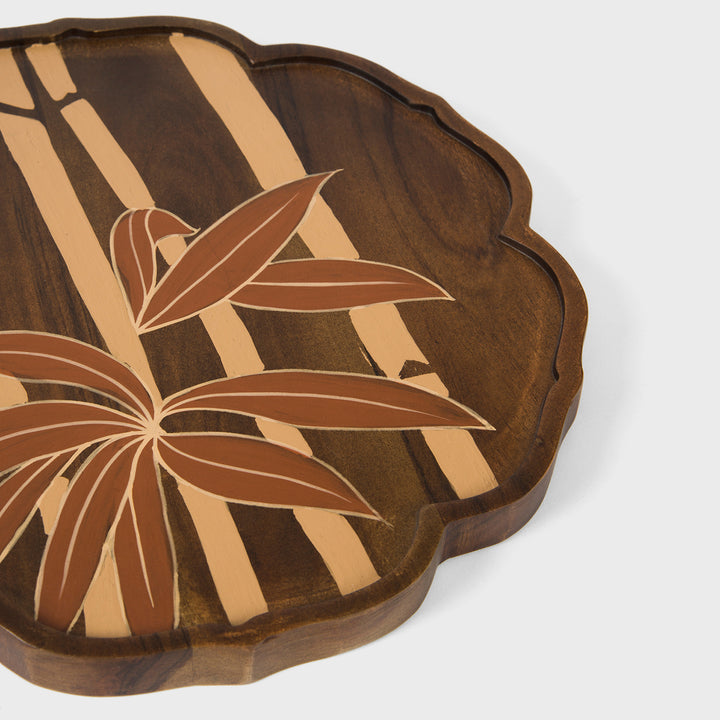 Close-up of scalloped border craftsmanship and hand painted cream and terracotta bamboo leaves on dark wood grain 