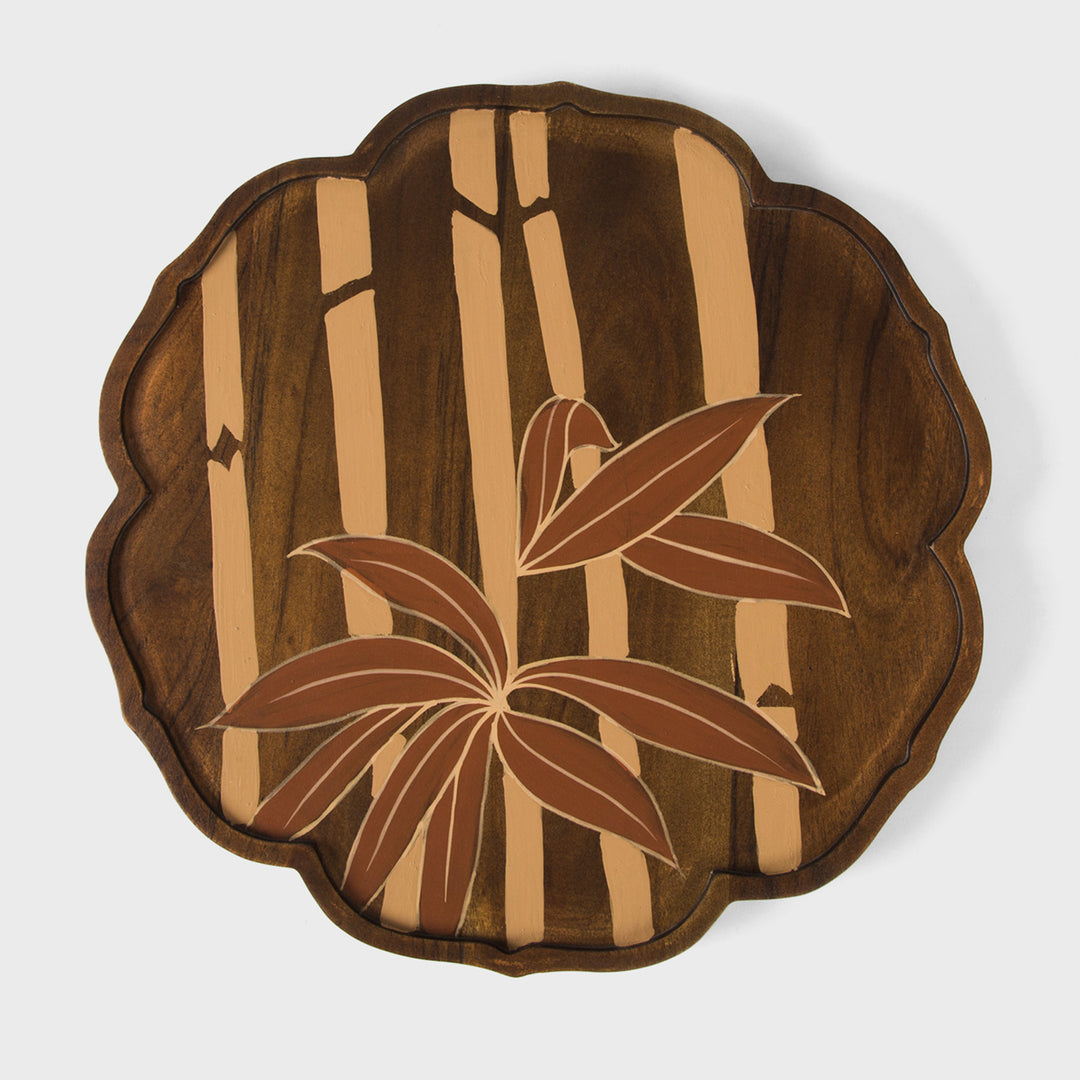 Close-up of scalloped border craftsmanship and hand painted cream and terracotta bamboo leaves on dark wood grain 