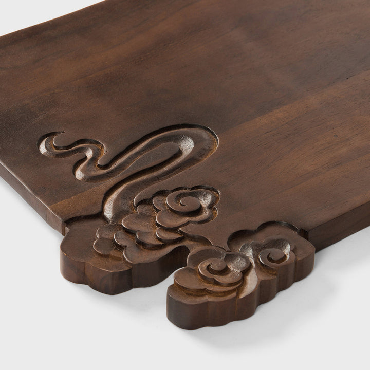 Close-up view of split-edge hand-carved cloud and wave details on dark acacia wood grain