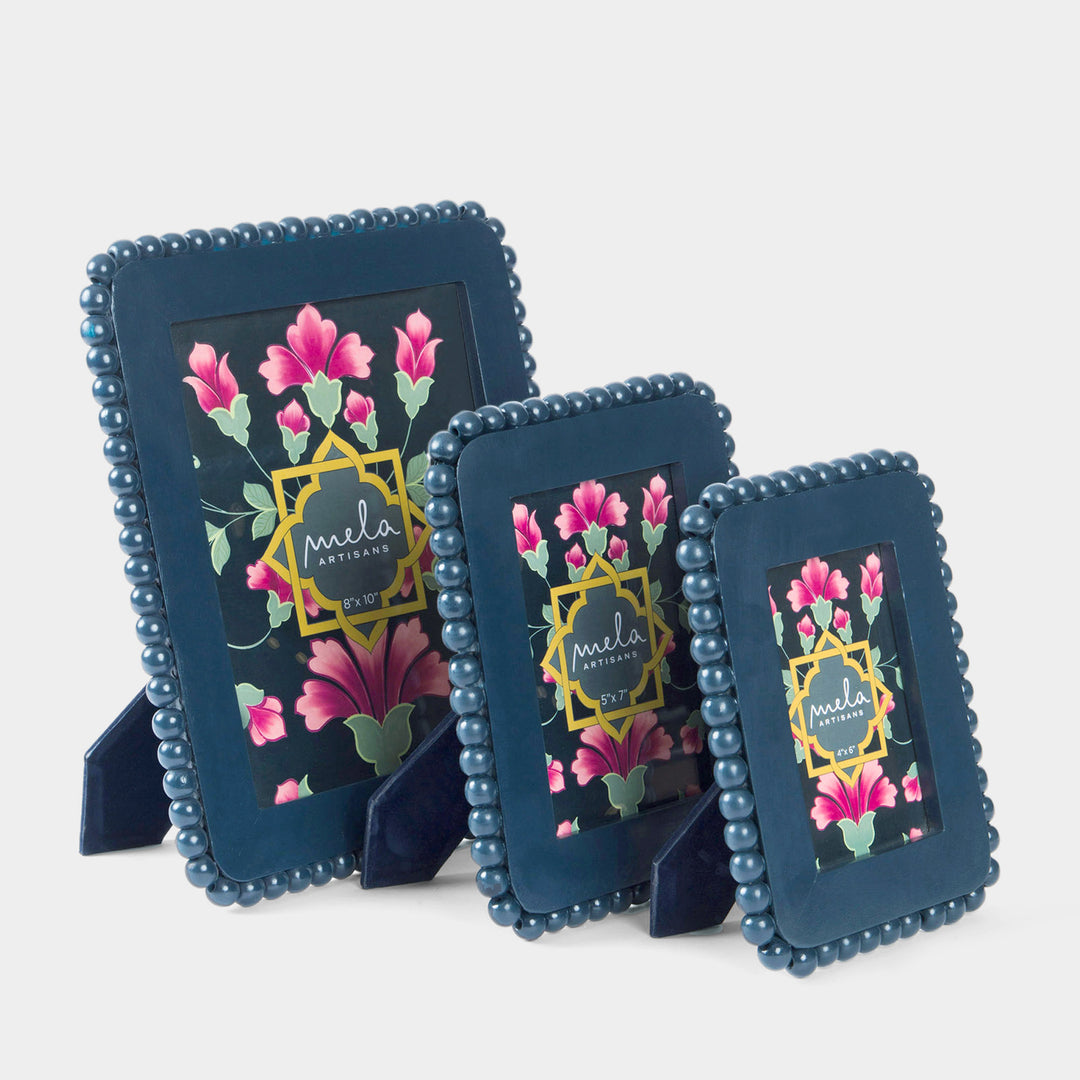 Three navy blue beaded picture frames with floral prints and gold accents, displayed on small stands.