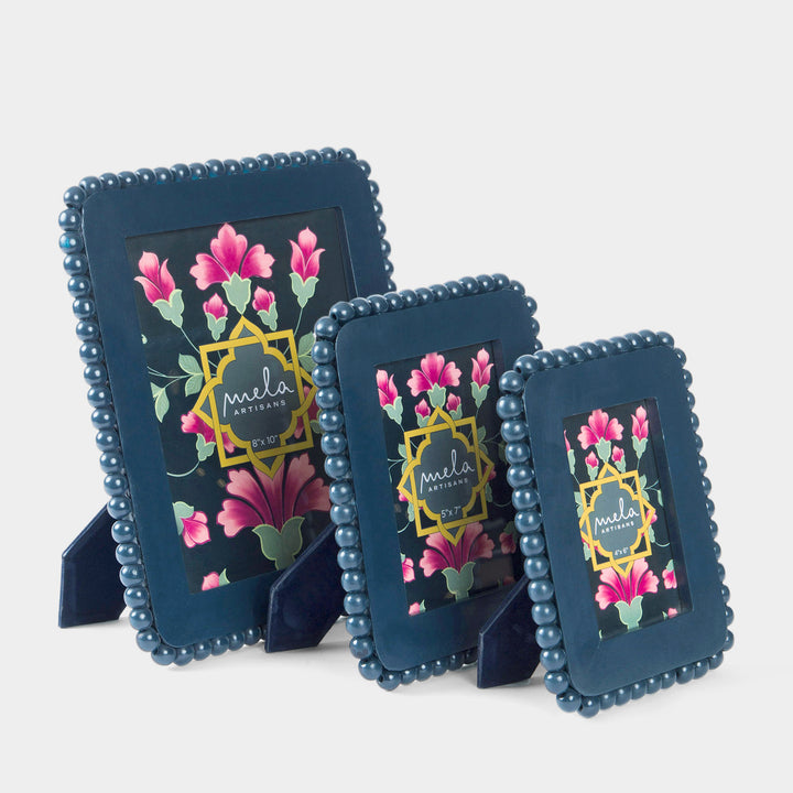 Three navy blue beaded picture frames with floral prints and gold accents, displayed on small stands.