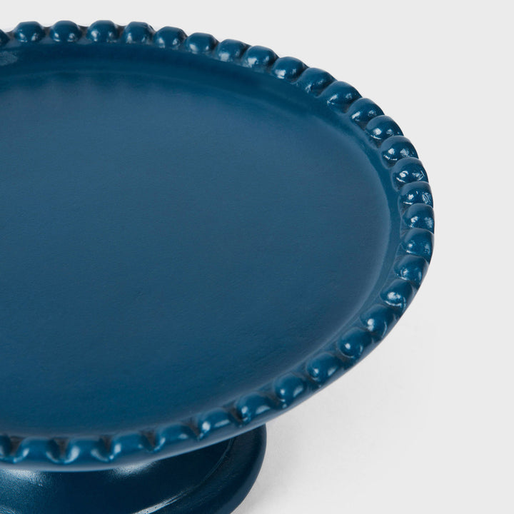 Close-up of the handcrafted terracotta cake stand highlighting its matte indigo glaze, raised beaded edge, and sculptural pedestal base.