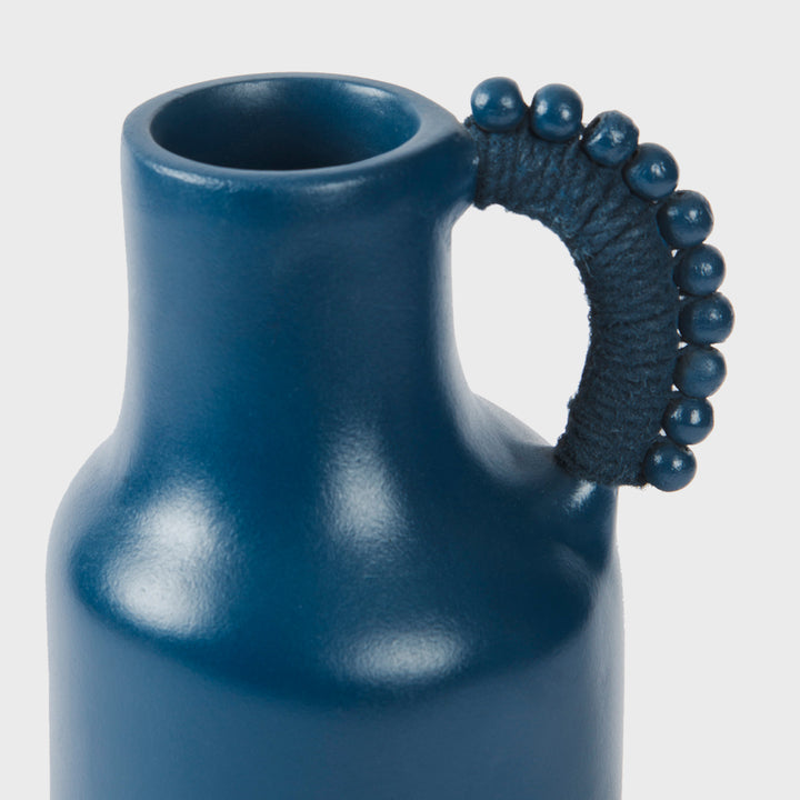 Close-up of the handcrafted terracotta pitcher showcasing its matte indigo glaze, sculptural silhouette, and beaded cord-wrapped handle.