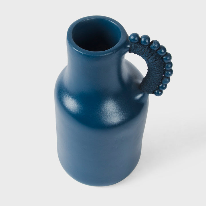Close-up of the handcrafted terracotta pitcher showcasing its matte indigo glaze, sculptural silhouette, and beaded cord-wrapped handle.