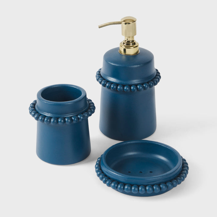 Three-piece blue bathroom accessory set including a pump bottle, a small cup, and a round dish, all with gold-tone hardware and beaded trim, shown on a light gray background.