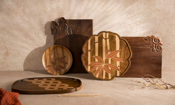A set of handcrafted wooden serving boards and trays with intricate inlay patterns, displayed against a textured beige wall.