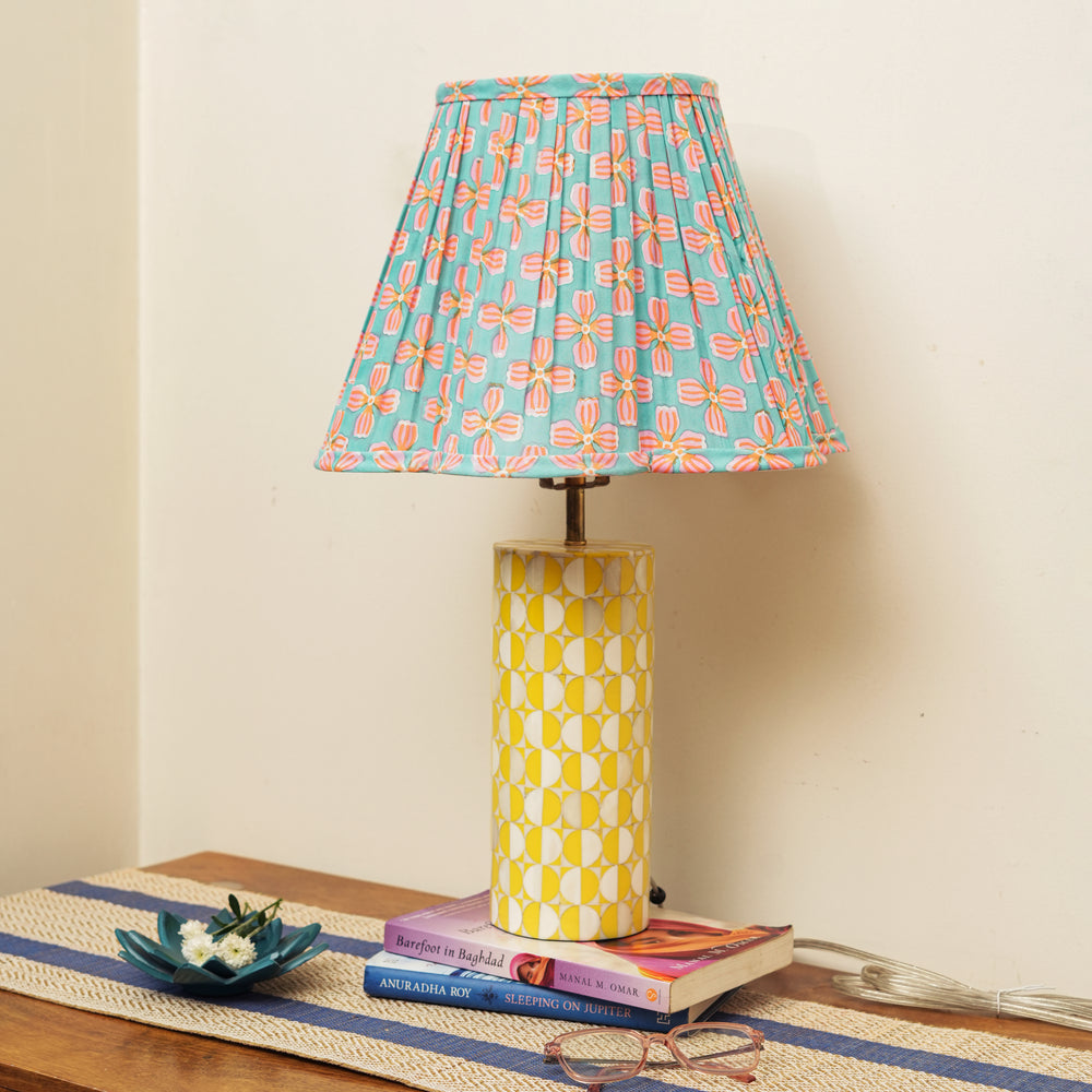 Lamp with a colorful floral-patterned shade on a table with books and a plant.