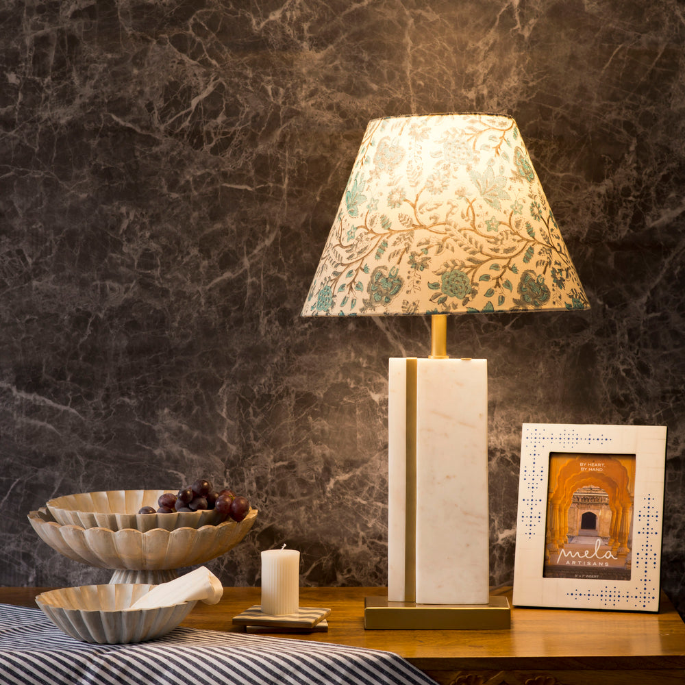 The Sculpta marble lamp base lit up in a cozy interior setting, highlighting the unique natural stone variations of the white marble.