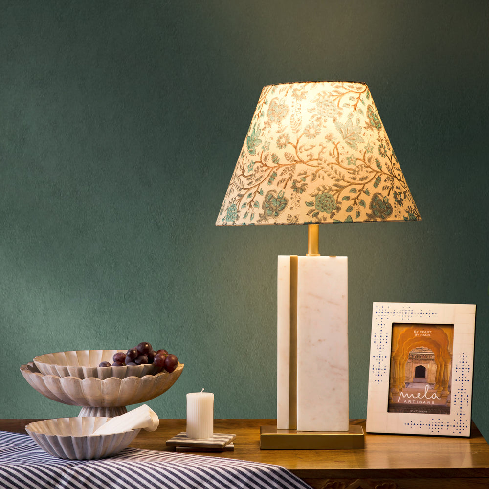 A warm, ambient living room scene featuring the Sculpta marble lamp on a side table next to a decorative bowl and book.