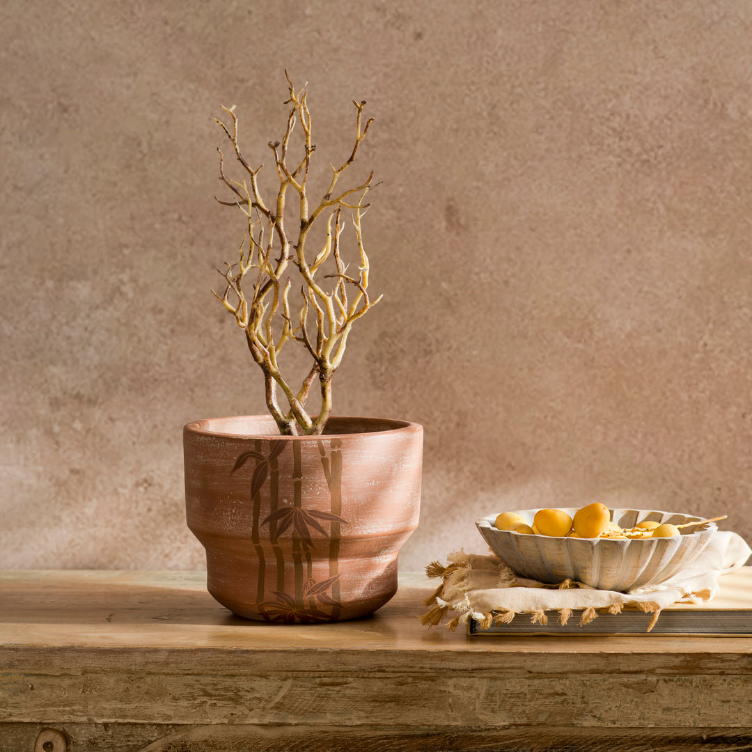 Japandi style terracotta plant pot sitting on an indoor wooden side table housing foliage 