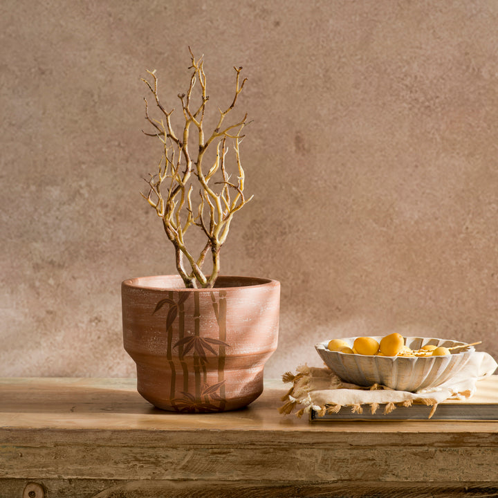 Japandi style terracotta plant pot sitting on an indoor wooden side table housing foliage 