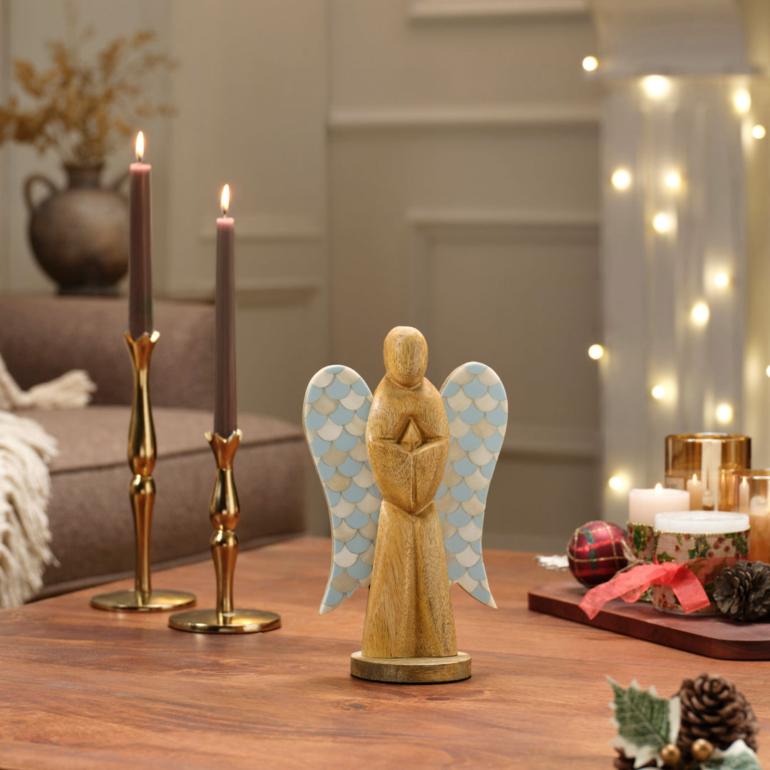 Hand carved wooden angel with teal blue bone inlay wings displayed on a festive holiday mantel