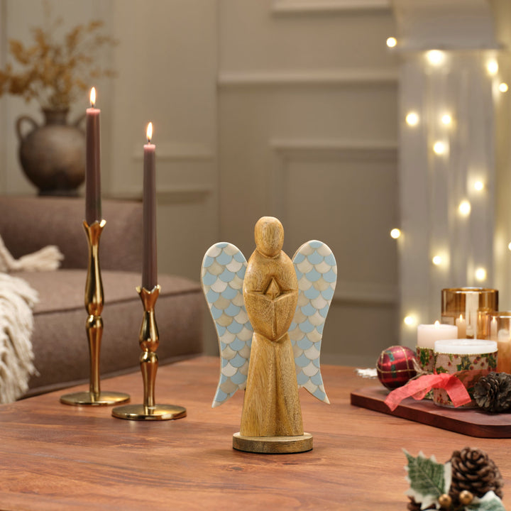 Hand carved wooden angel with teal blue bone inlay wings displayed on a festive holiday mantel