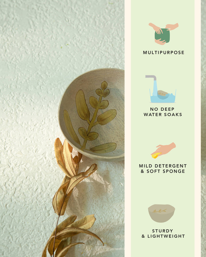 Ceramic dish with plant design on a textured surface, next to a green leafy branch.